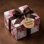 Pink cherry blossom floral wrapping paper on a gift box with a brown ribbon and Wrapped Studios tag.