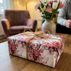 Pink cherry blossom floral wrapping paper by Wrapped Studios on a gift box tied with a gold bow.