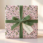 Pink botanical floral wrapping paper with a green velvet bow and 'With Love' gift tag by Wrapped Studios.