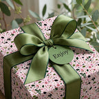 Pink floral wrapping paper with a sage green satin bow and 'Enjoy' gift tag by Wrapped Studios.