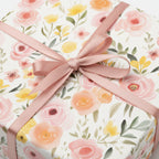 Floral wrapping paper featuring pink and yellow watercolor flowers, tied with a blush-colored ribbon bow.