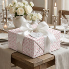 Elegant pink floral wedding wrapping paper on a gift box with a white satin bow by Wrapped Studios.