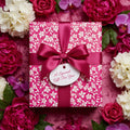 Elegant floral wrapping paper in pink and white, tied with a magenta satin ribbon, surrounded by roses and peonies.