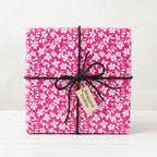 Bright pink floral wrapping paper on a square gift box tied with black string and a tag.