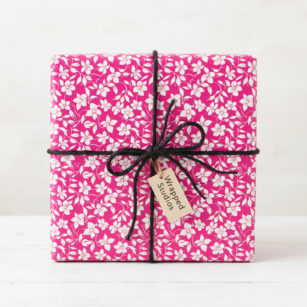 Bright pink floral wrapping paper on a square gift box tied with black string and a tag.