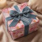 Elegant pink floral wrapping paper with blue velvet ribbon and "A Little Something" tag.