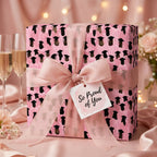 Elegant pink graduation wrapping paper with cap pattern and "So Proud of You" tag by Wrapped Studios.