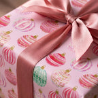 Pink Christmas wrapping paper with watercolor ornaments and satin ribbon bow by Wrapped Studios.