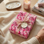 Wrapped Studios pink Christmas gift wrap with ornament pattern, ribbon bow, and "With Love" tag.