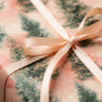 Blush pink Christmas wrapping paper with watercolor pine trees and satin ribbon bow by Wrapped Studios.