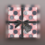 Square gift box wrapped in modern pink polka dot wrapping paper with a grey velvet ribbon and gift tag.