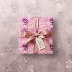 Square gift wrapped in pink floral wrapping paper with ribbon and tag.