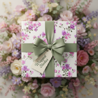 Elegant floral wrapping paper with purple and pink blossoms, tied with a sage green ribbon and bow, perfect for a wedding or birthday gift.