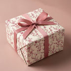 Elegant pink floral wrapping paper on a gift box with a dusty rose ribbon bow by Wrapped Studios.