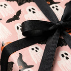 Pink Halloween wrapping paper with ghosts and bats, tied with a black bow by Wrapped Studios.