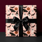 Cute pink Halloween wrapping paper with ghosts and bats, tied with a black satin bow by Wrapped Studios.