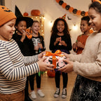 Kids exchanging a gift in pink ghost Halloween wrapping paper with an orange bow by Wrapped Studios.