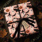 Cute pink Halloween wrapping paper with ghosts and pumpkins, tied with a black ribbon by Wrapped Studios.