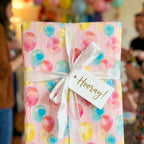 Pink birthday wrapping paper with watercolor balloons and a white ribbon by Wrapped Studios.