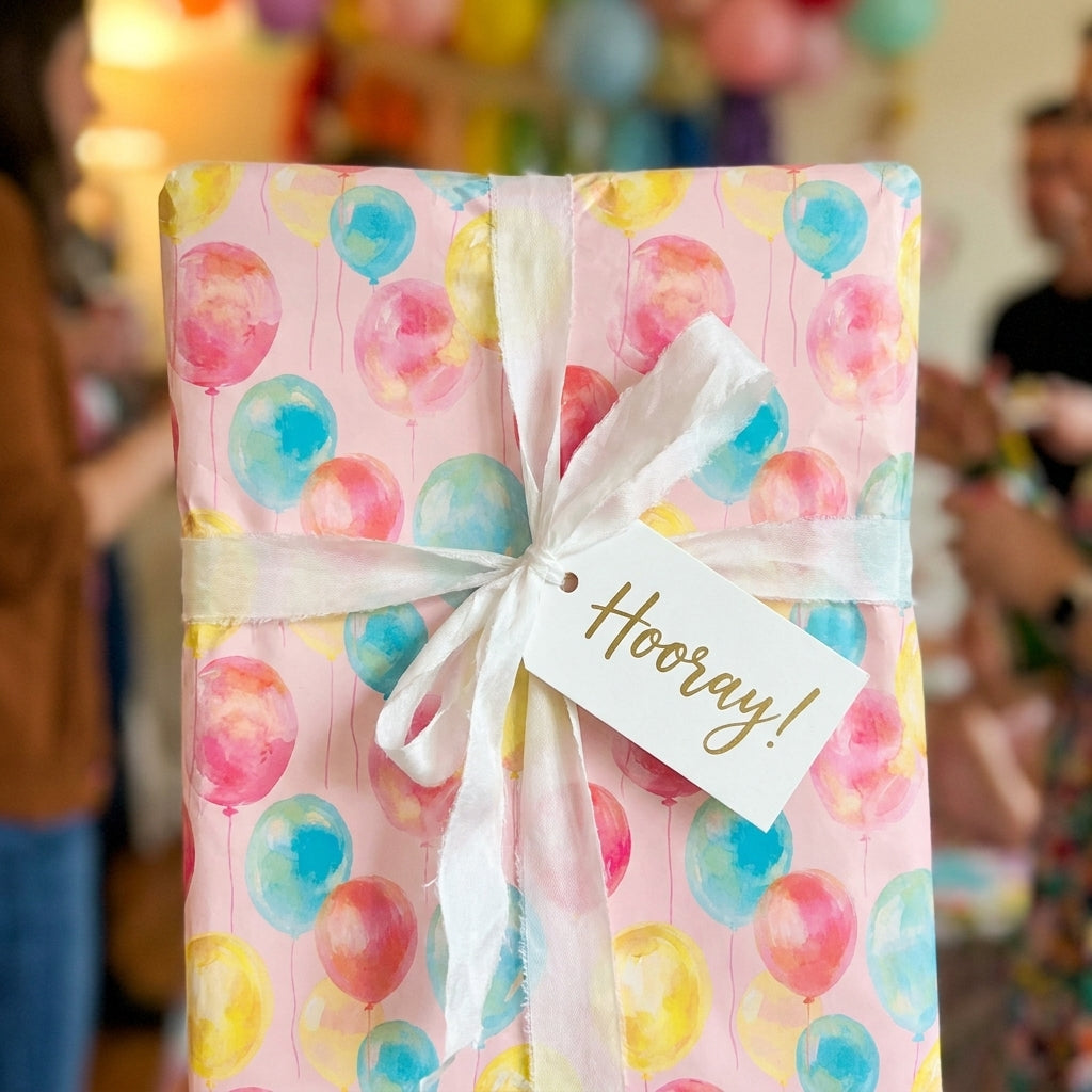 Pink birthday wrapping paper with watercolor balloons and a white ribbon by Wrapped Studios.