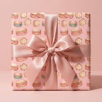Pink baby shower wrapping paper with watercolor drums and a satin bow, by Wrapped Studios.