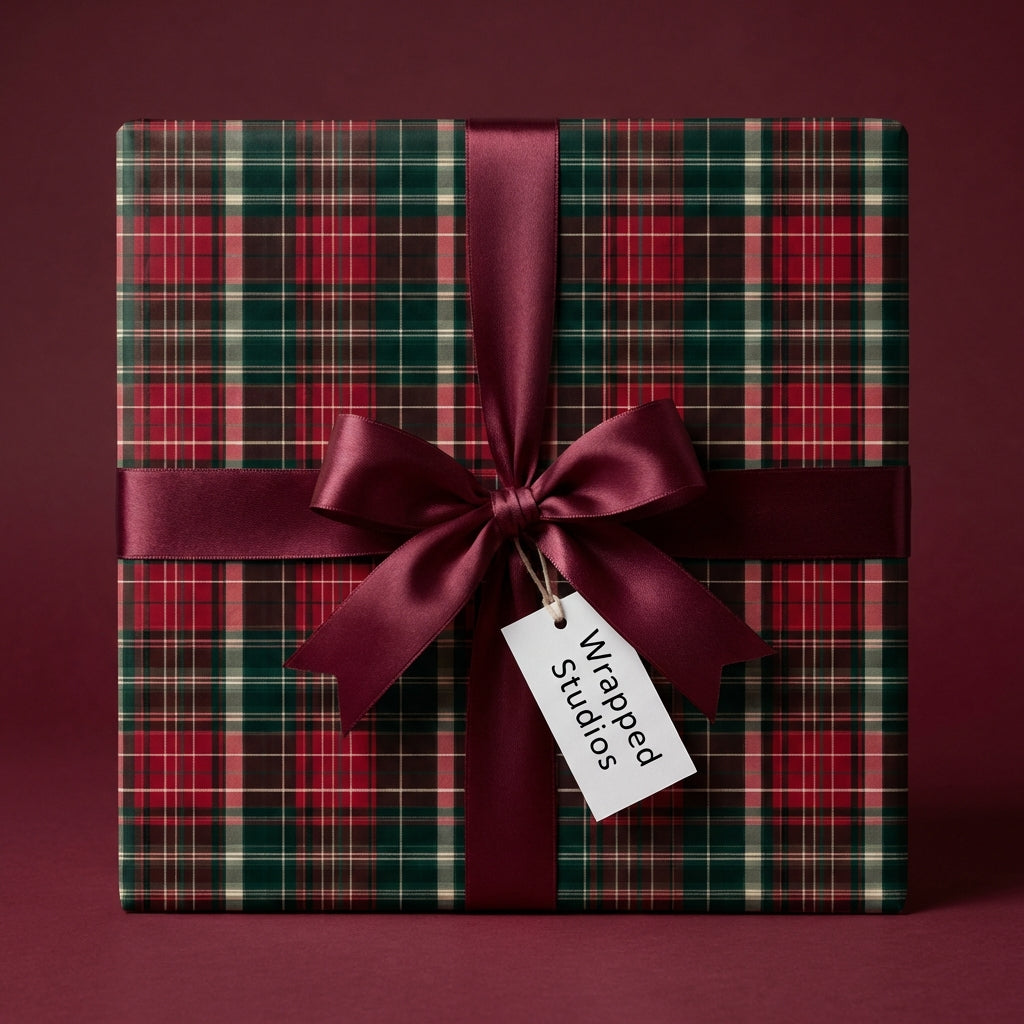 Square gift box in classic red and green plaid Christmas wrapping paper with satin burgundy ribbon and bow.