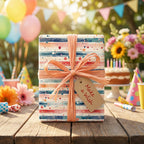 Striped "Make a Wish" birthday gift wrapped with peach ribbon. Party balloons and cake in background.