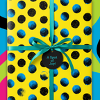 Yellow birthday wrapping paper with blue and black dots, teal ribbon and "A Spot of Joy!" tag.