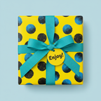 Bright yellow birthday wrapping paper with bold blue and black dots, tied with a turquoise ribbon and "Enjoy!" tag.