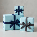 Light blue wrapping paper on gift boxes with navy and gray ribbon bows.