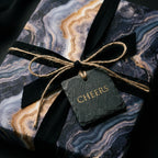 Luxury navy and gold marble wrapping paper with a black ribbon and Cheers tag by Wrapped Studios.
