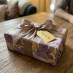 Elegant purple and gold marbled wrapping paper with a satin bow and gift tag, from Wrapped Studios.