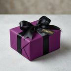Elegant gift wrapped in solid purple wrapping paper with a black satin ribbon and bow.
