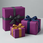 Elegant gifts wrapped in solid purple wrapping paper with gray, navy, and gold ribbons.
