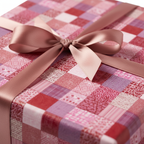 Red and pink patchwork pattern wrapping paper with a light brown satin ribbon and bow, perfect for a cozy Christmas or birthday gift.