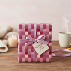 Pink patchwork plaid wrapping paper with a light purple ribbon and "Wrapped with Love" tag, perfect for a cozy birthday or holiday gift.