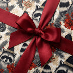 Woodland raccoon Christmas wrapping paper with a red satin bow by Wrapped Studios.