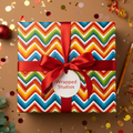 Colorful chevron birthday wrapping paper on a square gift box with a bright red ribbon.