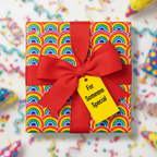 Square gift with rainbow pattern wrapping paper, bright red ribbon, and “For Someone Special” tag.