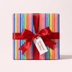 Colorful rainbow stripe birthday wrapping paper with a red satin bow by Wrapped Studios.