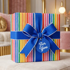 Rainbow striped birthday wrapping paper with a large blue bow and gift tag, by Wrapped Studios.