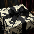 Elegant gift wrapped in cream paper with a black raven and tree branch pattern, tied with a black grosgrain ribbon.