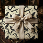 Elegant gift wrapped in cream paper with a unique raven and branch design, tied with a rustic beige ribbon.