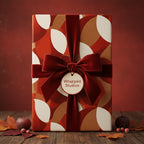 Elegant gift box with rust colored geometric wrapping paper, tied with a velvet ribbon and surrounded by autumn leaves.