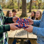 Red, white, and blue camo wrapping paper on a gift being exchanged outdoors by Wrapped Studios.