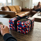 Modern red and blue camo wrapping paper on a gift box with a black bow by Wrapped Studios.