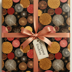 Elegant gift wrapped in modern geometric wrapping paper with gold, red, and white circle patterns, tied with a peach satin ribbon.