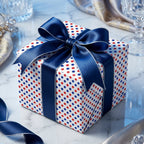 Red and blue polka dot wrapping paper with a navy satin bow on a gift box, by Wrapped Studios.