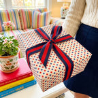 Red and blue polka dot wrapping paper with a striped ribbon bow by Wrapped Studios, held by a woman.