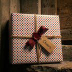 Red and blue polka dot wrapping paper with a rustic twine bow and Cheers tag by Wrapped Studios.